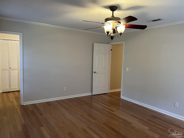 empty room with crown molding, visible vents, a textured ceiling, wood finished floors, and baseboards