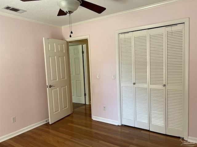 unfurnished bedroom featuring dark wood-style flooring, a closet, visible vents, ornamental molding, and a textured ceiling