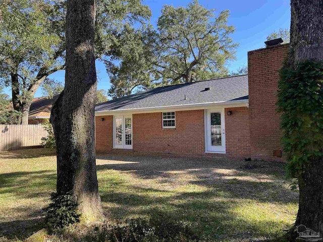 rear view of house featuring french doors, a chimney, fence, a yard, and brick siding