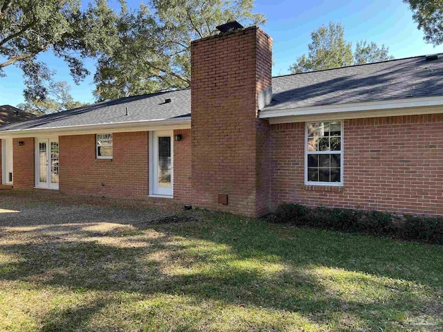 back of property featuring brick siding, a yard, a chimney, and roof with shingles