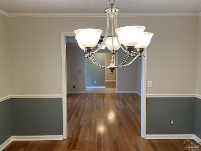 unfurnished dining area with an inviting chandelier, a textured ceiling, baseboards, and wood finished floors