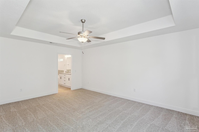 carpeted spare room featuring a raised ceiling and ceiling fan