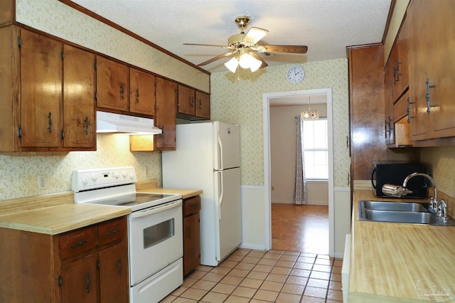 kitchen featuring a textured ceiling, under cabinet range hood, white appliances, a sink, and wallpapered walls