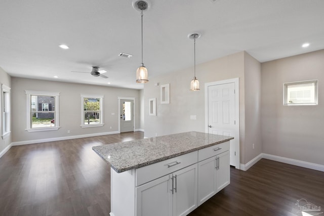 kitchen featuring pendant lighting, dark wood-type flooring, white cabinetry, a center island, and light stone counters