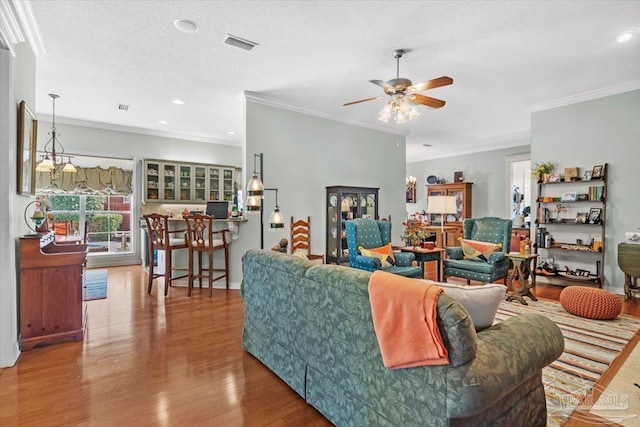 living room with ceiling fan, a textured ceiling, wood-type flooring, and ornamental molding