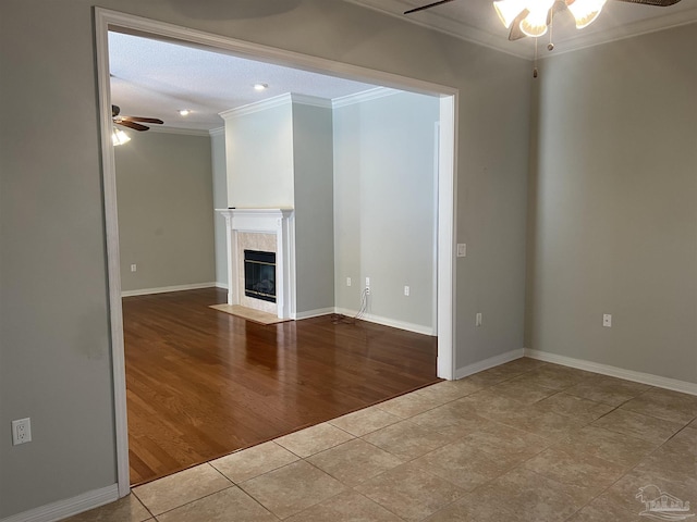 unfurnished living room featuring ceiling fan, a tiled fireplace, tile patterned floors, baseboards, and ornamental molding
