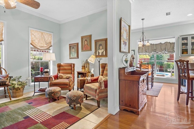 living area featuring light hardwood / wood-style flooring, ornamental molding, a wealth of natural light, and ceiling fan with notable chandelier