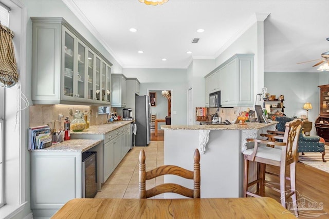 kitchen featuring wine cooler, stainless steel fridge, light tile patterned floors, ornamental molding, and light stone counters