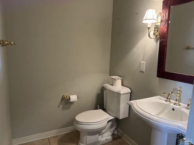 half bathroom featuring toilet, tile patterned floors, a sink, and baseboards