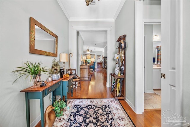 corridor with baseboards, visible vents, ornamental molding, and wood finished floors