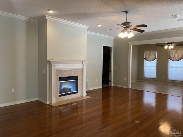unfurnished living room with ceiling fan, visible vents, a tiled fireplace, crown molding, and wood finished floors