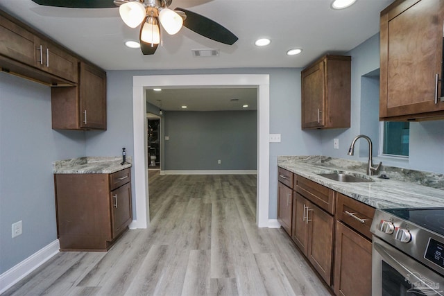 kitchen with electric stove, sink, ceiling fan, light stone counters, and light hardwood / wood-style flooring