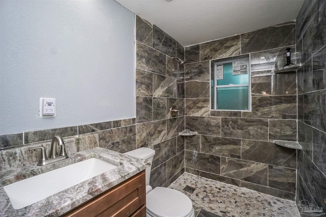 bathroom featuring vanity, tile walls, toilet, and tiled shower