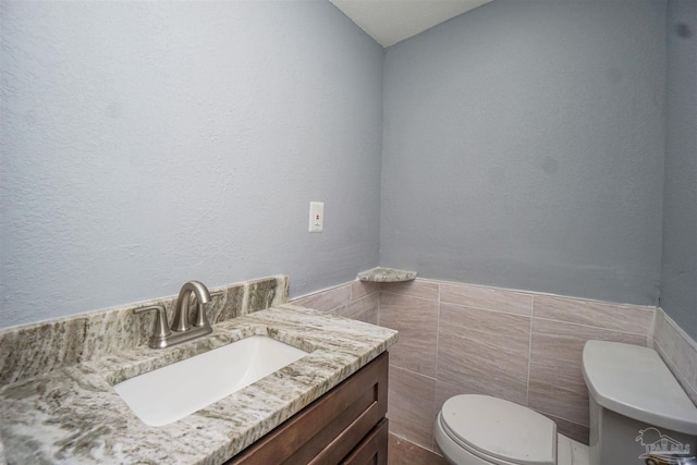 bathroom featuring vanity, tile walls, and toilet