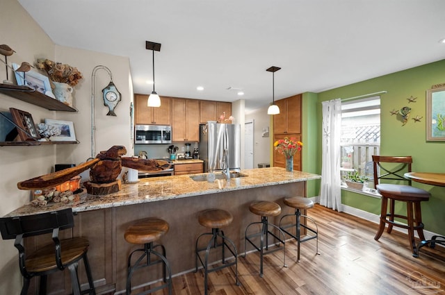 kitchen with a kitchen breakfast bar, stainless steel appliances, light hardwood / wood-style floors, and decorative light fixtures