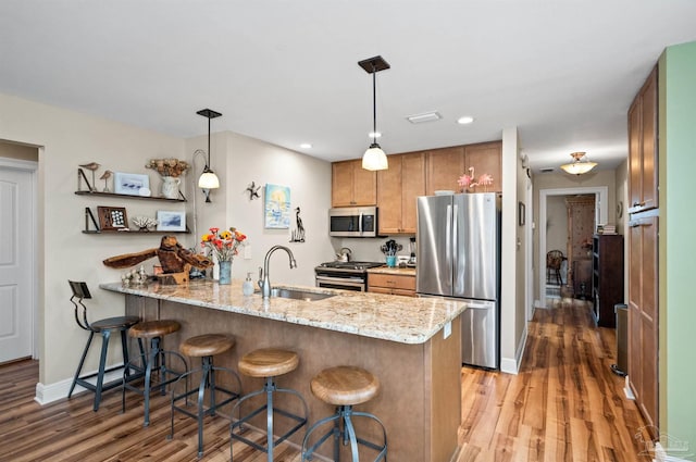 kitchen featuring light hardwood / wood-style floors, kitchen peninsula, stainless steel appliances, decorative light fixtures, and light stone countertops