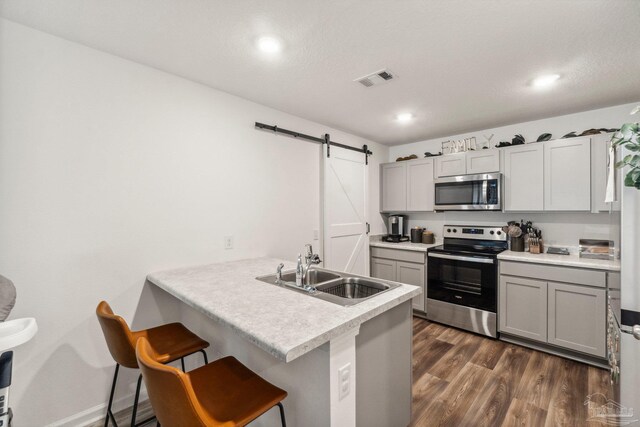 4348 Jitterbug St, Milton, FL 32583 - kitchen with appliances with stainless steel finishes, a sink, a barn door, a peninsula, and a kitchen bar