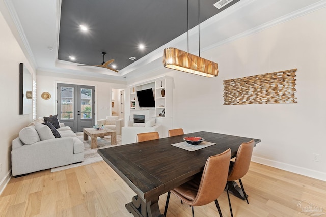 dining space with ornamental molding, a tray ceiling, french doors, and light hardwood / wood-style floors