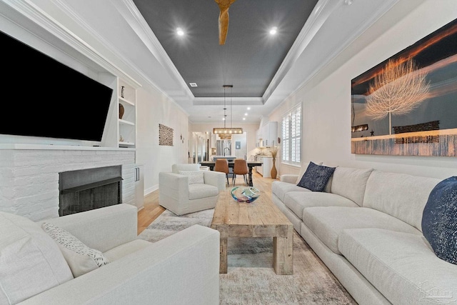 living room with a stone fireplace, light hardwood / wood-style flooring, a raised ceiling, and crown molding