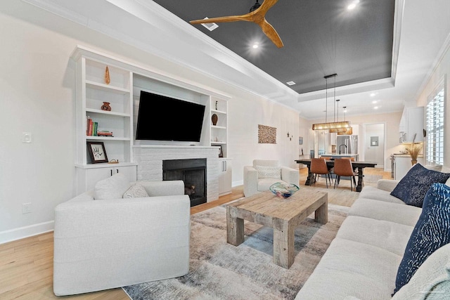 living room with a fireplace, a raised ceiling, and light hardwood / wood-style flooring