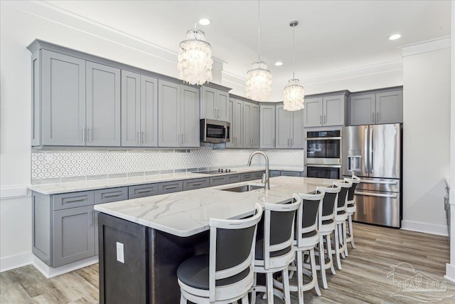 kitchen featuring tasteful backsplash, gray cabinetry, appliances with stainless steel finishes, a sink, and light stone countertops