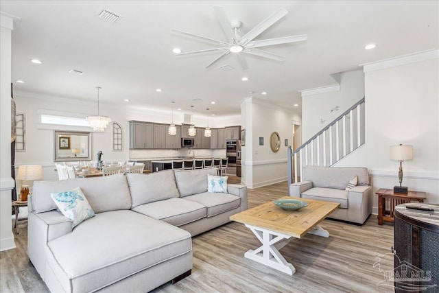 living room featuring light wood-style floors, stairway, visible vents, and crown molding