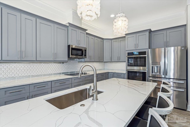 kitchen featuring a sink, appliances with stainless steel finishes, gray cabinets, backsplash, and an inviting chandelier