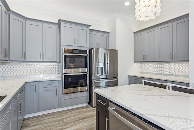 kitchen with stainless steel appliances, backsplash, light stone counters, and gray cabinetry