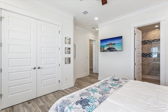 bedroom with ensuite bathroom, wood finished floors, visible vents, baseboards, and ornamental molding