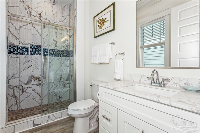 bathroom featuring toilet, a marble finish shower, wood finished floors, and vanity