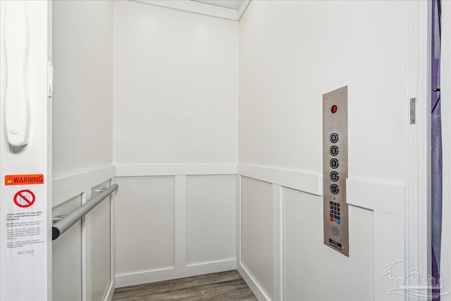 interior space featuring a wainscoted wall, a decorative wall, wood finished floors, and elevator