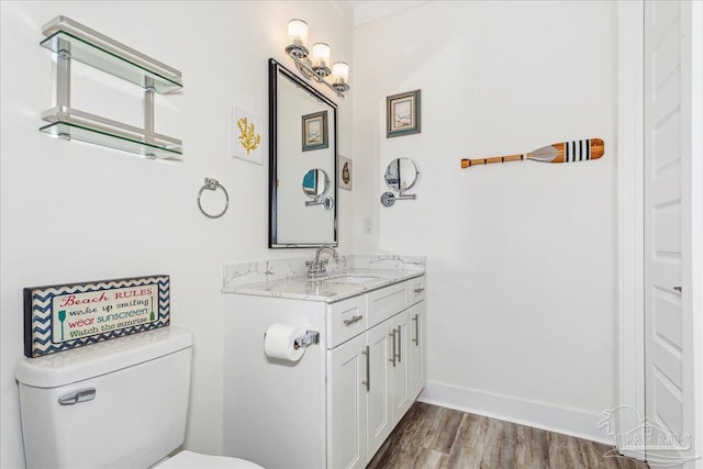 half bathroom with baseboards, vanity, toilet, and wood finished floors