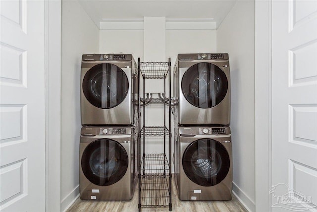 clothes washing area with laundry area, wood finished floors, stacked washer and clothes dryer, and baseboards