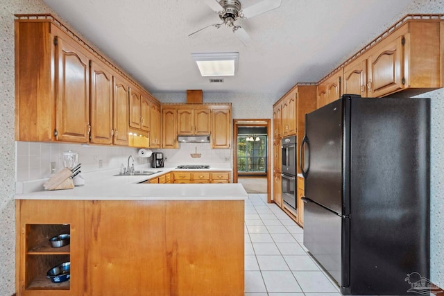 kitchen featuring stainless steel gas stovetop, kitchen peninsula, black refrigerator, light tile patterned flooring, and sink