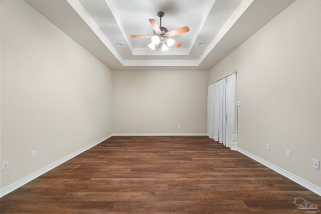 unfurnished room with ceiling fan, dark hardwood / wood-style floors, and a tray ceiling