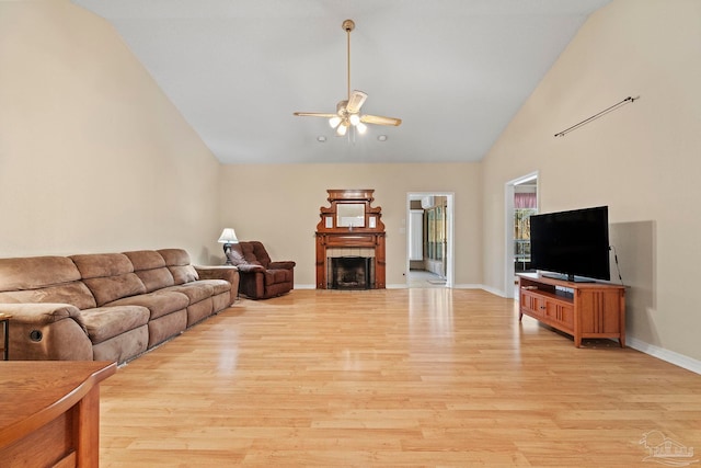 living room with ceiling fan, lofted ceiling, a fireplace, and light hardwood / wood-style flooring