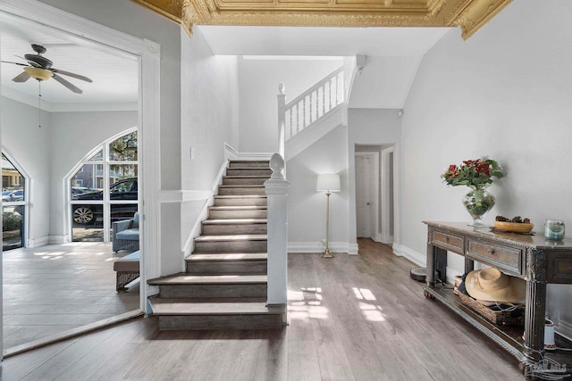 staircase featuring a high ceiling, ornamental molding, hardwood / wood-style floors, and ceiling fan