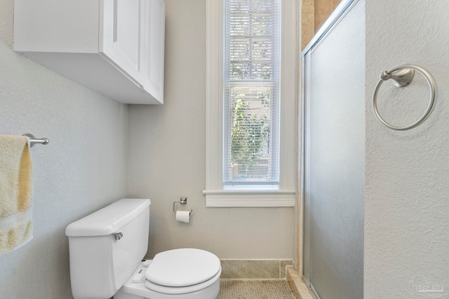 bathroom with toilet, a shower with door, and a wealth of natural light