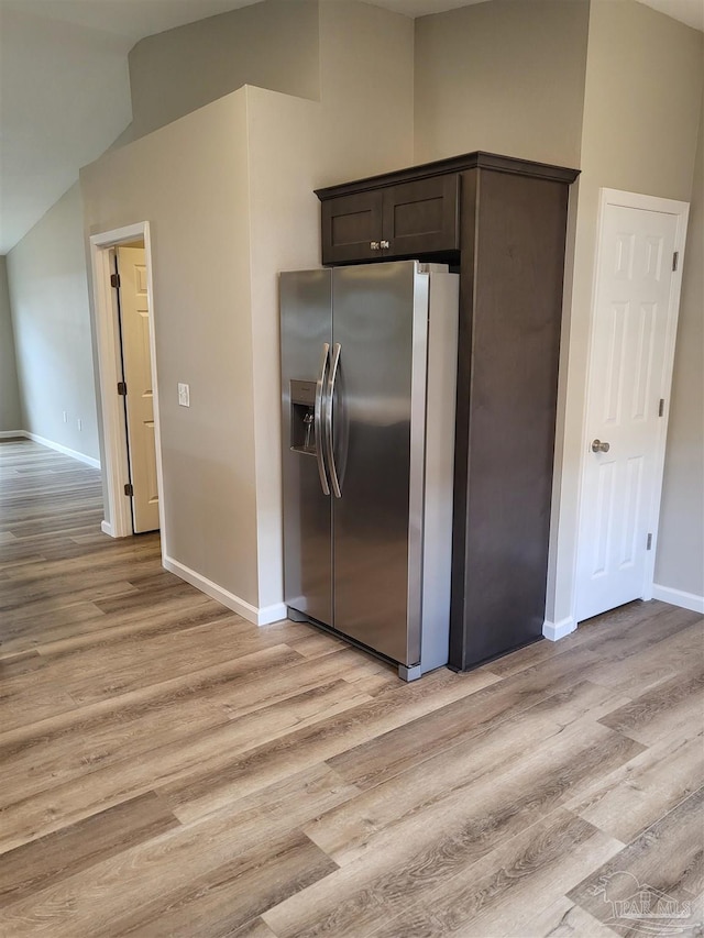 kitchen featuring stainless steel fridge, vaulted ceiling, dark brown cabinets, and light hardwood / wood-style floors