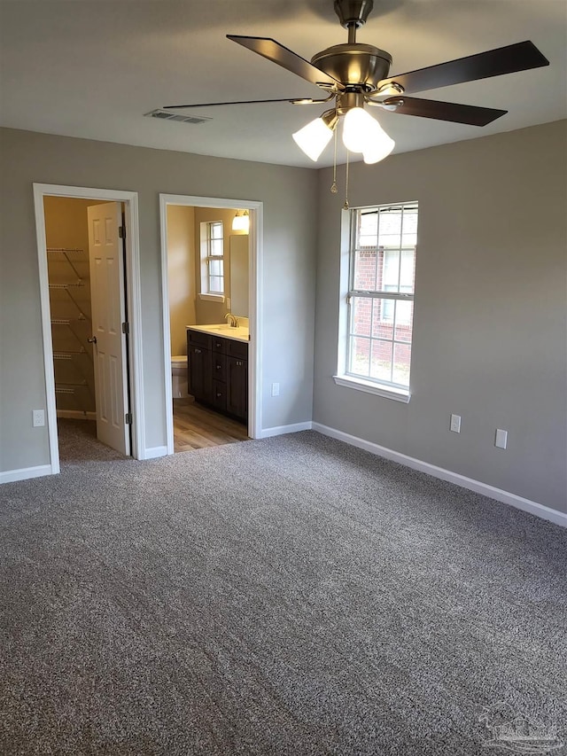 unfurnished bedroom featuring carpet flooring, a walk in closet, ensuite bath, a closet, and ceiling fan