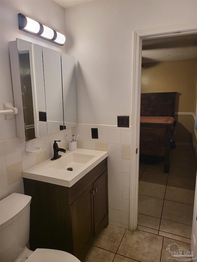 bathroom with vanity, tile patterned flooring, toilet, and tile walls