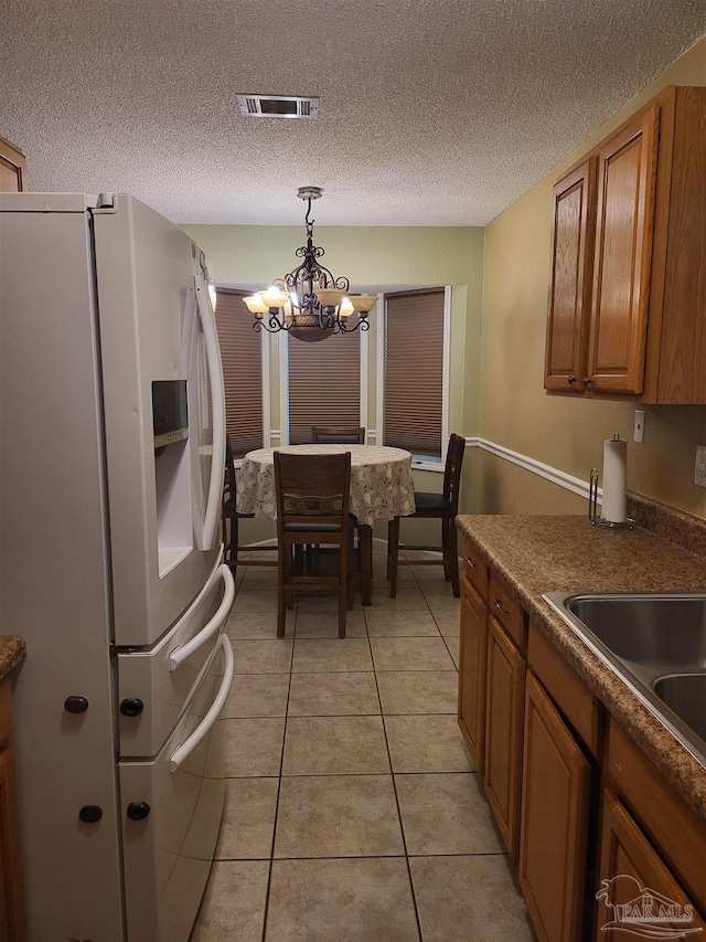 kitchen with light tile patterned floors, white refrigerator with ice dispenser, a textured ceiling, decorative light fixtures, and a chandelier