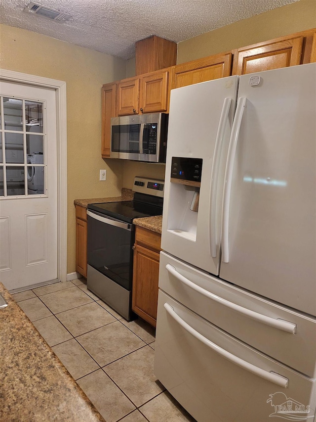 kitchen with stainless steel appliances, a textured ceiling, and light tile patterned flooring