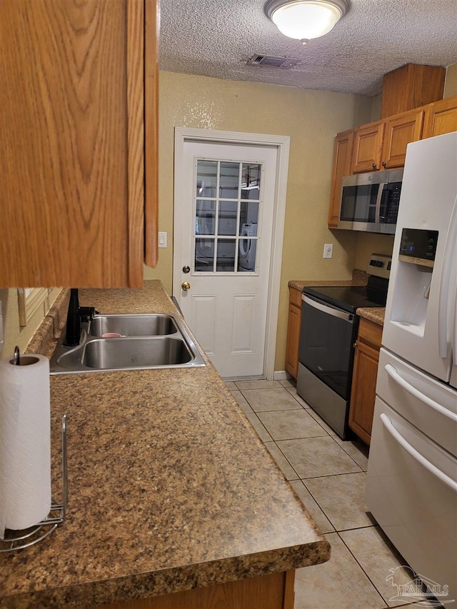 kitchen featuring appliances with stainless steel finishes, sink, light tile patterned floors, and a textured ceiling