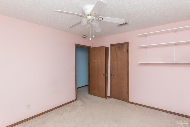 unfurnished bedroom featuring light carpet, a textured ceiling, and ceiling fan