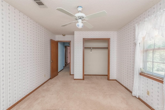 unfurnished bedroom featuring ceiling fan, light colored carpet, a closet, and a textured ceiling