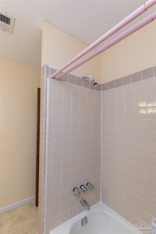 bathroom with tile patterned flooring, tiled shower / bath combo, and a textured ceiling