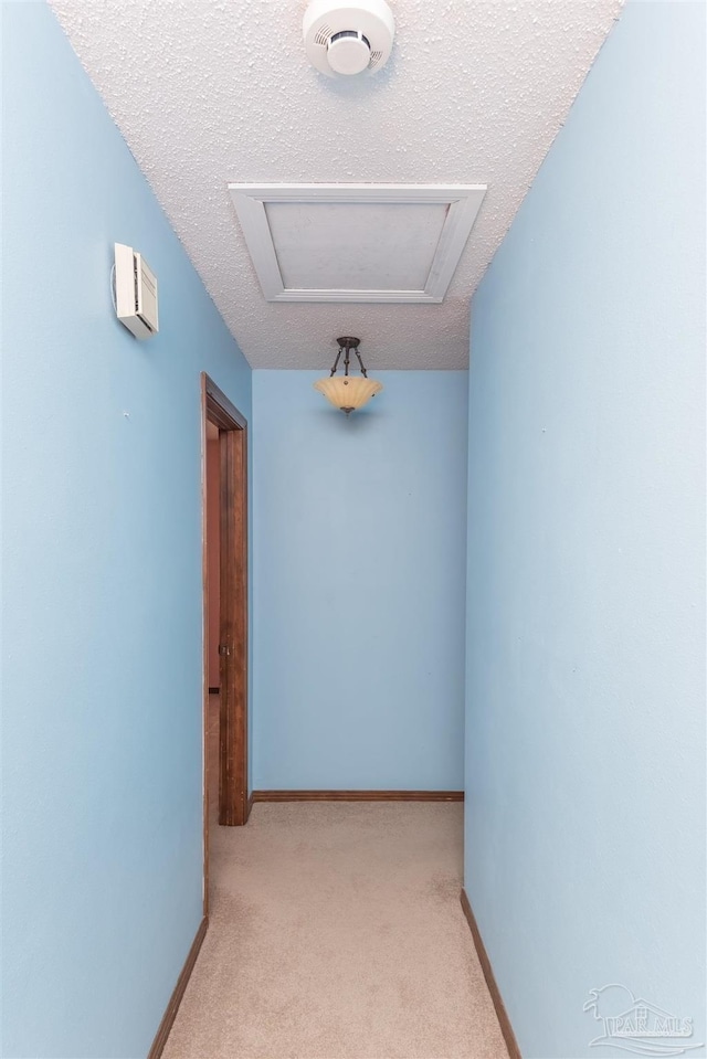 corridor with light carpet and a textured ceiling