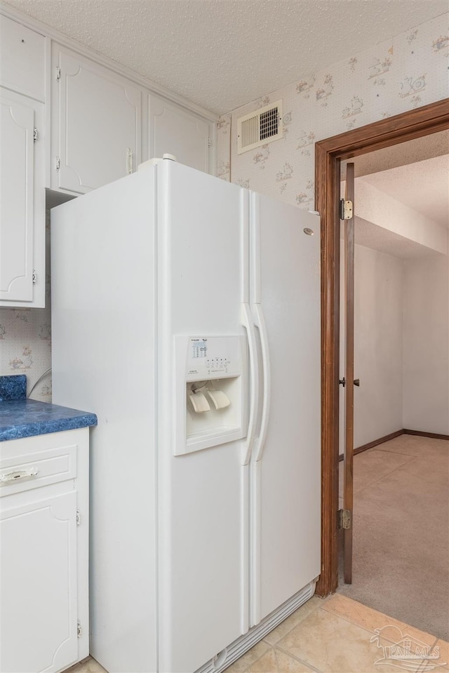 kitchen featuring white cabinetry, white refrigerator with ice dispenser, light carpet, and a textured ceiling