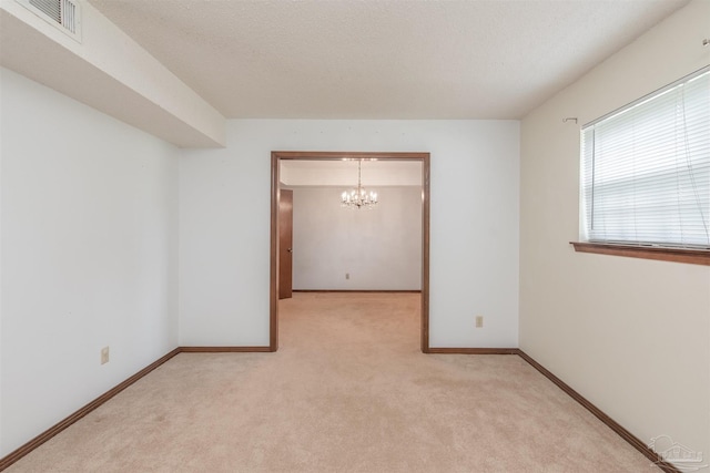 spare room featuring an inviting chandelier, light carpet, and a textured ceiling